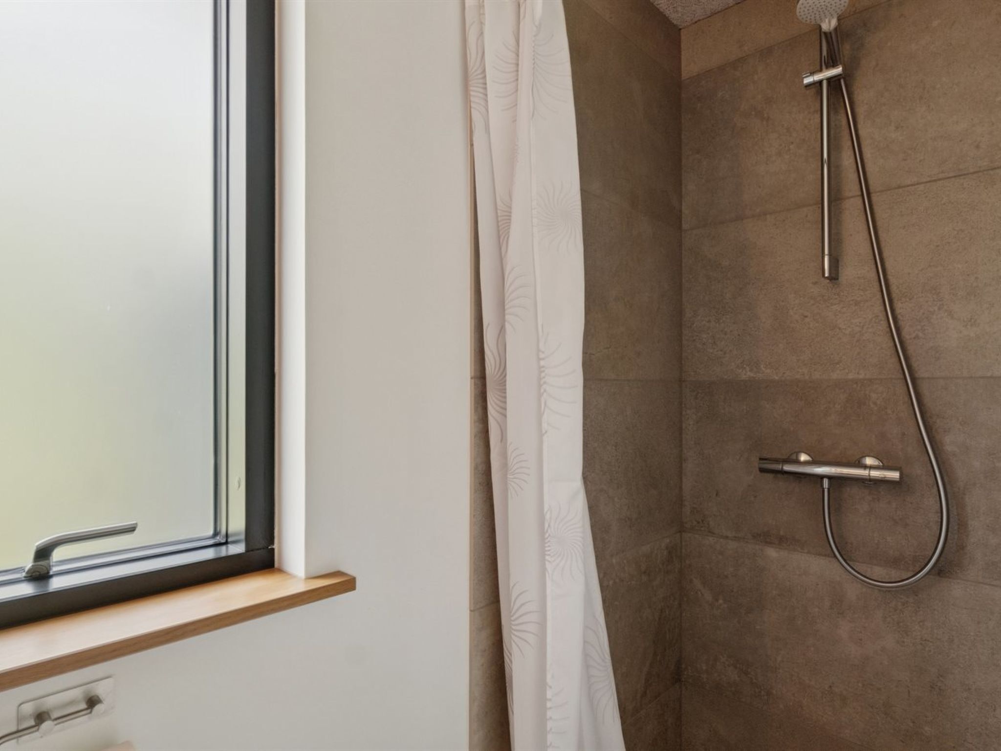 A bathroom with a shower, a window, and a towel rack.