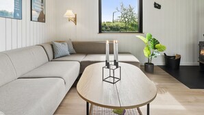 Un saló modern amb un sofà modular, una taula de centre rodona de fusta, una làmpada penjada a la paret, una finestra gran amb vistes i una xemeneia.
