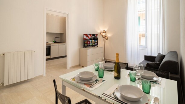Un salon moderne avec une table à manger pour quatre personnes, un canapé, un téléviseur et un lustre.