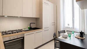 Une cuisine moderne équipée d’une cuisinière à gaz, d’un four et d’un évier, avec des meubles de couleur claire et un coin repas comprenant une table dressée pour deux personnes.
