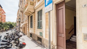 Une rangée de motos garées, l’entrée d’un immeuble avec une porte, et un panneau indiquant un espace de stationnement.