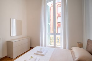 A bedroom with a bed, a dresser, a lamp, and a window with a view of buildings.
