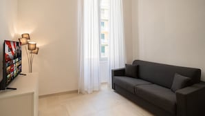 Un salon avec un canapé, un téléviseur et une fenêtre avec des rideaux.