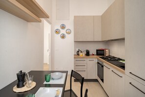 Une cuisine compacte équipée d’un four à micro-ondes, d’une cuisinière et d’une machine à café. On y trouve une table à manger avec des chaises, ainsi qu’un petit îlot central doté d’une machine à café.