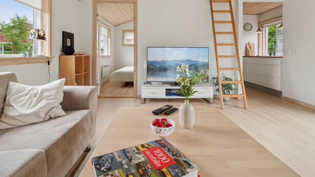 Een moderne woonkamer met een televisie, een bank, een salontafel met een tijdschrift en uitzicht op de omgeving door een raam.