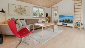 Een moderne woonkamer met een houten plafond, een rode stoel, een bank, een salontafel, een televisie en een ladder.