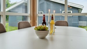 Een eettafel met een schaal fruit, twee kaarsen en twee flessen drank.