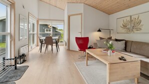 Een moderne woonkamer met een houten plafond, een eethoek met een tafel en stoelen, een rode fauteuil, een bank en een salontafel.