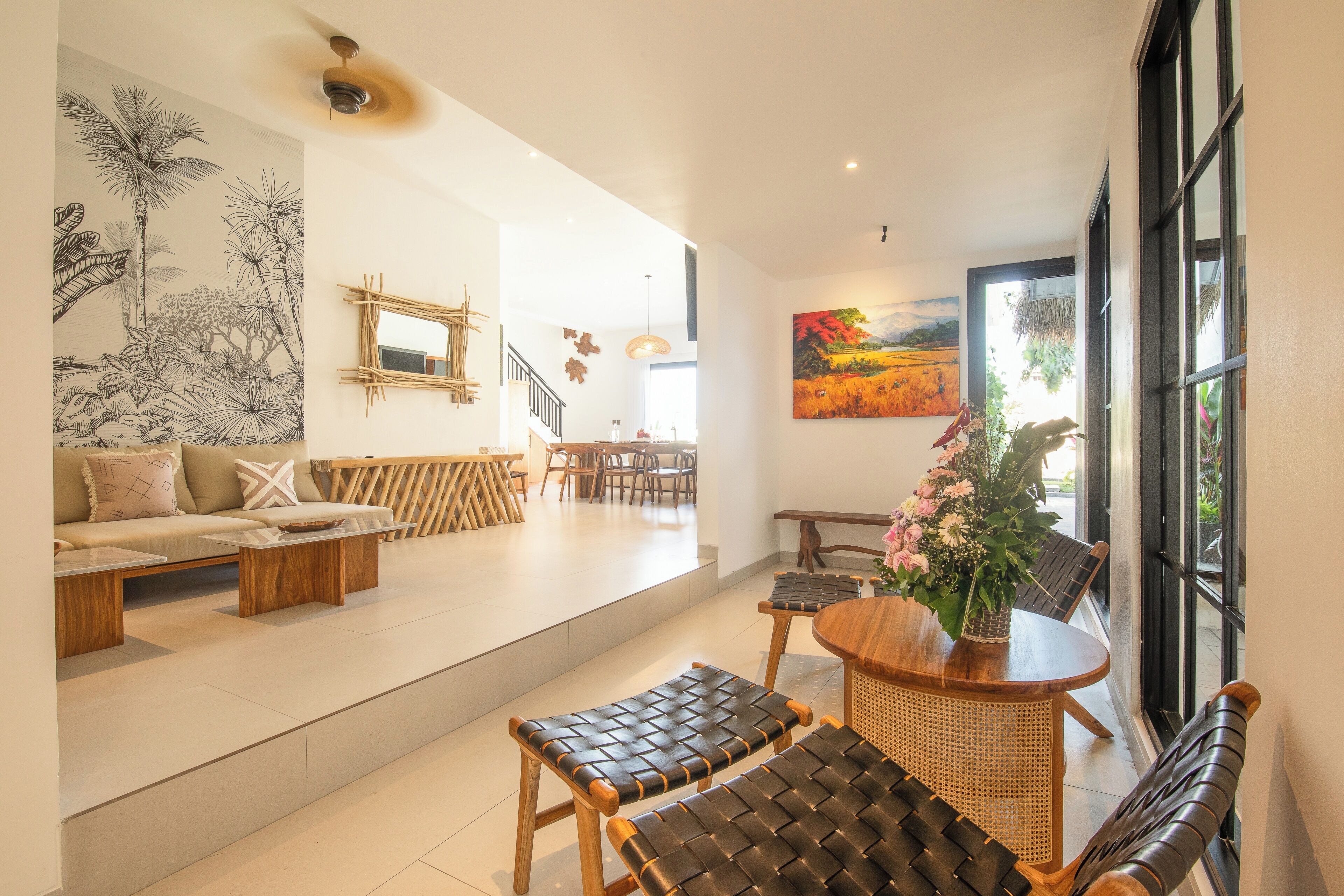 A spacious living area with a sofa, coffee table, and seating area. There is a staircase leading to another level, and a dining area with chairs and a table.