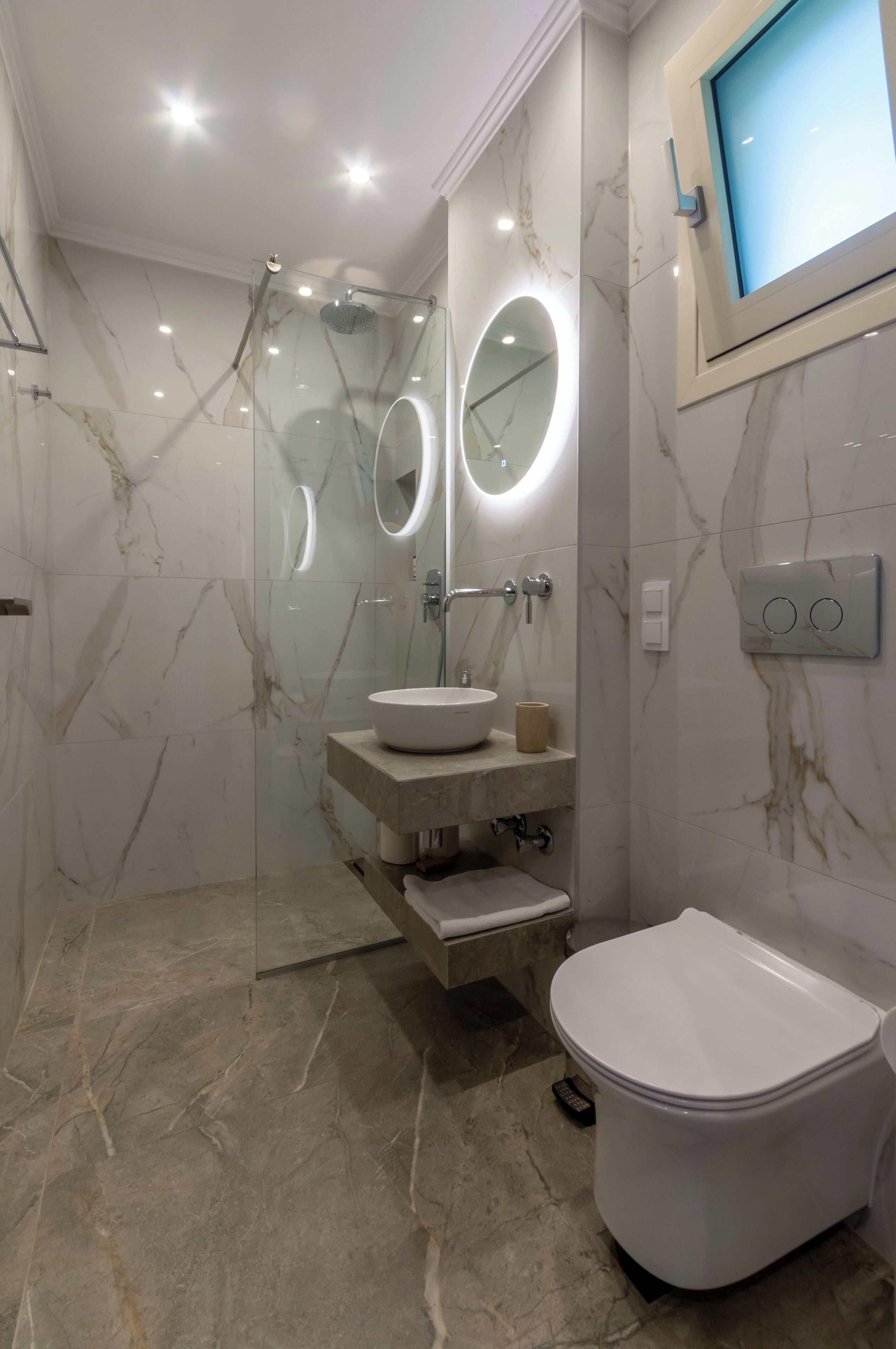 A modern bathroom with a glass-enclosed shower, a round mirror, a white sink, and a toilet.