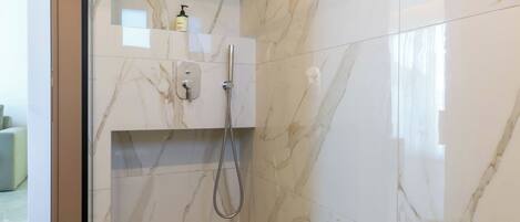 Baño con ducha, azulejos de mármol y mampara de vidrio.