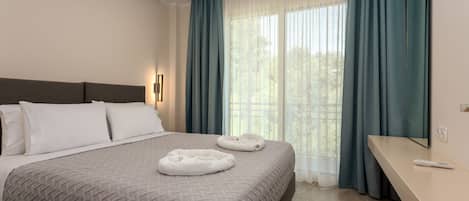 A modern hotel room with a large bed, a bedside table, a mirror, and a window with curtains.