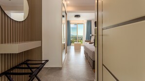 A hotel room with a bed, a small table, a mirror, and a view of the outdoors. - Corfelia Seaview Suites (Corfu)