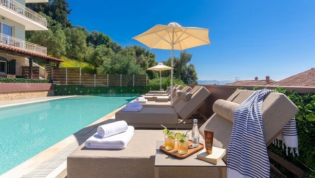 A poolside area with lounge chairs, umbrellas, and a bar area with drinks. - Corfelia Seaview Suites (Corfu)