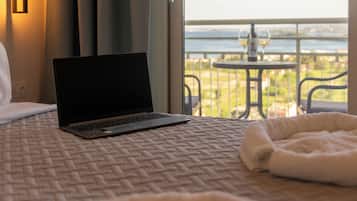 Una laptop sobre la cama, con vistas a un balcón y una mesa con vasos y una botella.