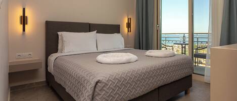 A modern hotel room with a large bed, two wall-mounted lights, a balcony with a view, and a small table.