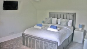 Une chambre à coucher avec un lit, des tables de chevet et un téléviseur fixé au mur.