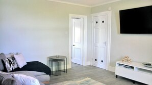 Un salon avec un canapé gris, une petite table ronde, un meuble blanc et un téléviseur à écran plat fixé au mur.