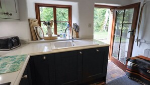 A kitchen with a large island, a sink, and a window overlooking a garden. - Chapel Cottage (Cleator)