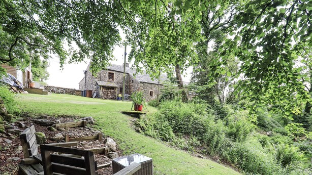 A stone house with a grassy yard, a wooden bench, and a potted plant. - Chapel Cottage (Cleator)