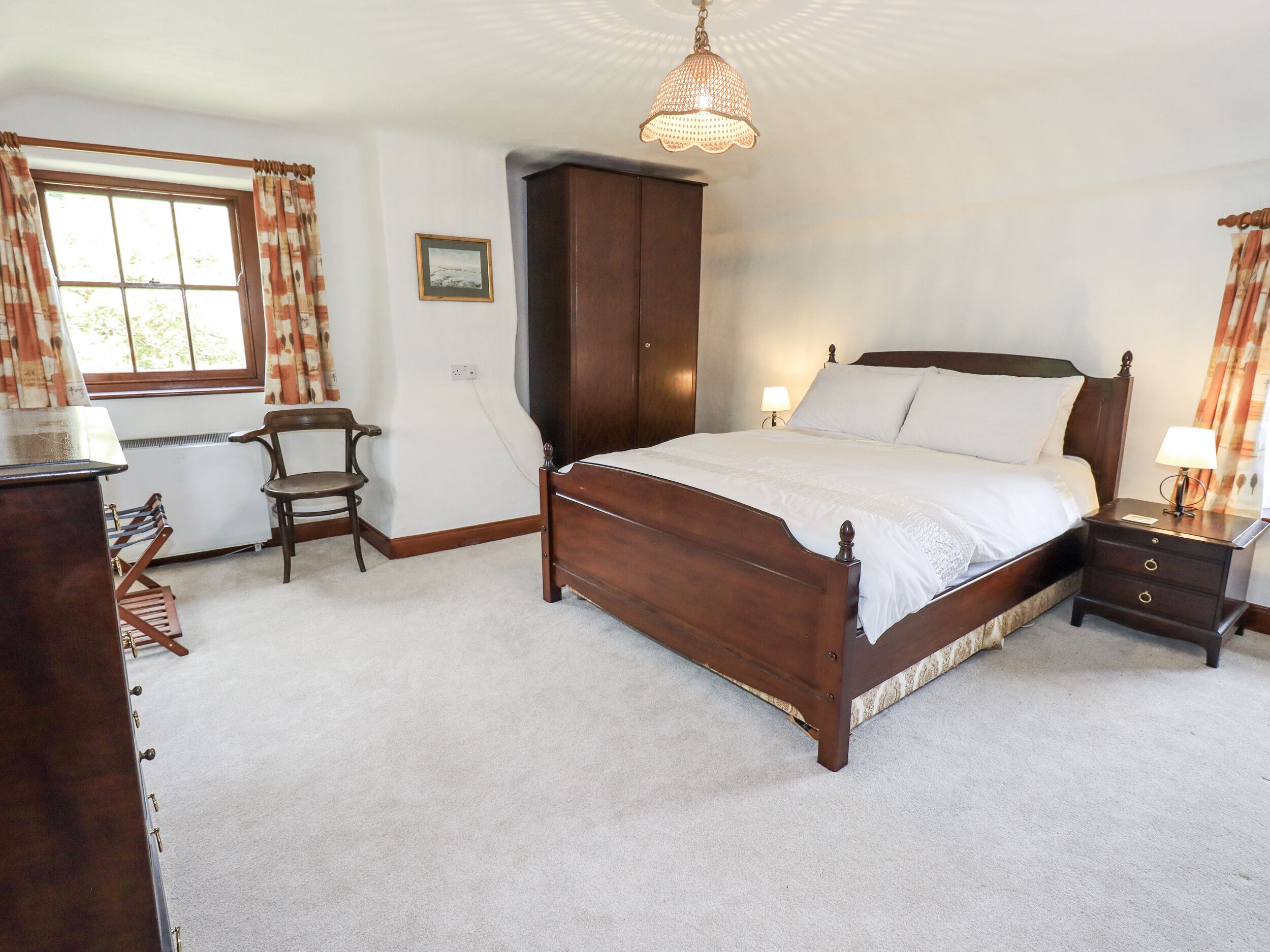 Een slaapkamer met een houten bed, nachtkastje, stoel, kledingkast en raam met gordijnen.