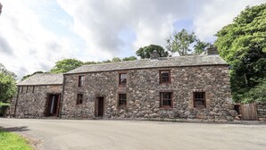 A stone building with multiple windows and a door, surrounded by greenery. - Chapel Cottage (Cleator)