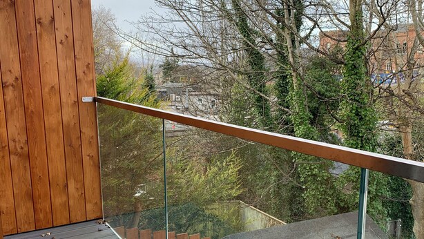 Um deck de madeira com guarda-corpo de vidro, com vista para a paisagem urbana.