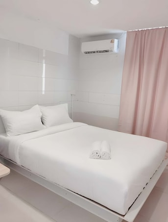 A neatly made bed with white linens and towels, a white headboard, and an air conditioning unit on the wall.