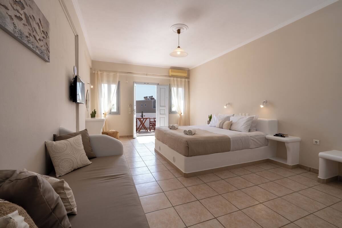 A modern bedroom with a large bed, a sofa, a bedside table, and a view of the outside.