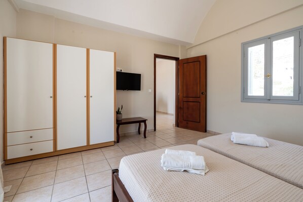 A bedroom with two beds, a wardrobe, a television, and a window.
