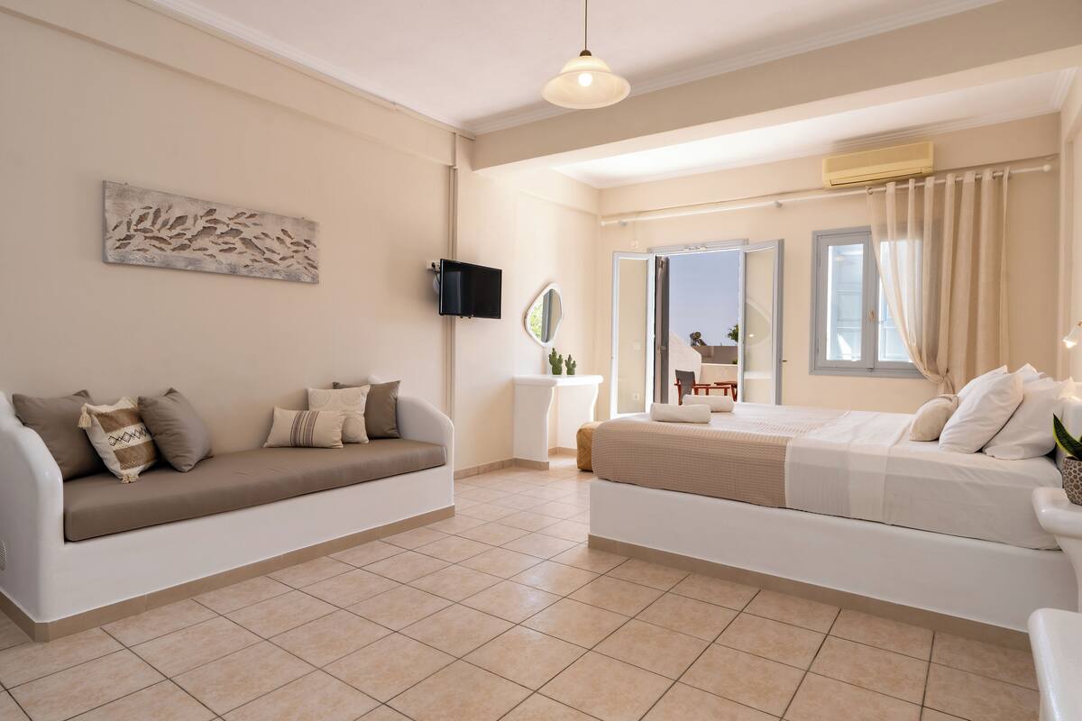 A modern bedroom with a sofa, a bed, a TV, and a window.