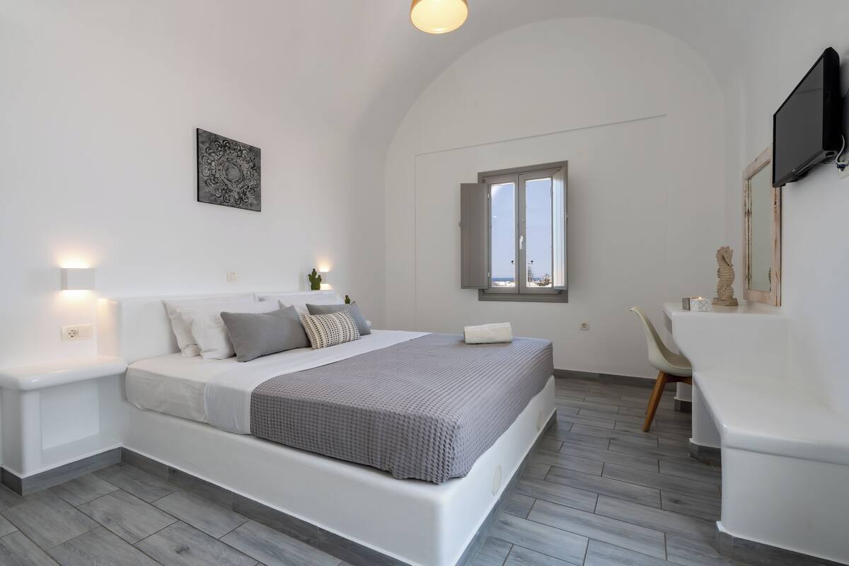 A modern bedroom with a bed, bedside tables, a desk, and a TV.
