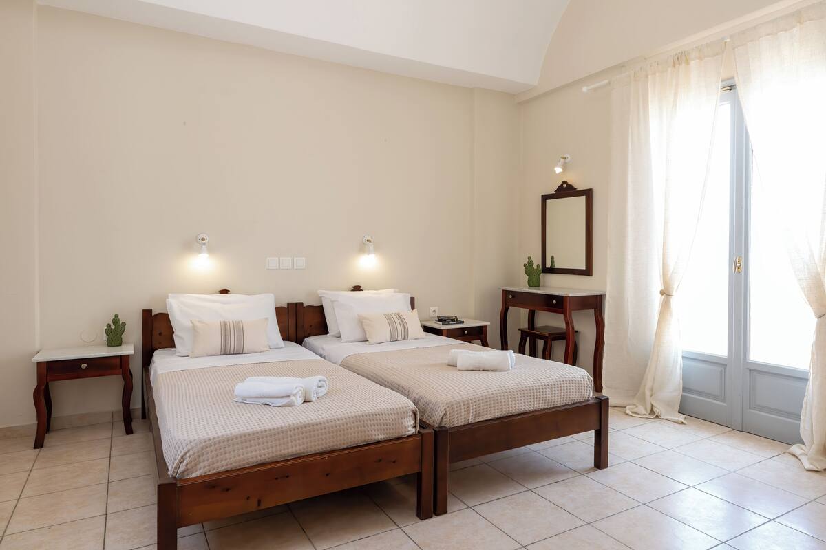 A hotel room with two single beds, a wooden nightstand, a small table, and a mirror on the wall.