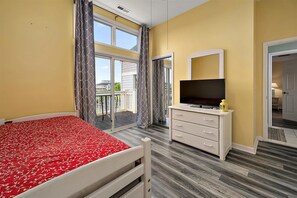 Une chambre à coucher avec un lit, un téléviseur posé sur une commode, un balcon avec des rideaux et une vue sur l’extérieur.