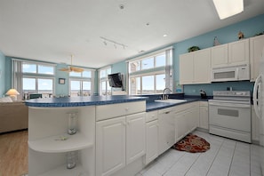 Una cocina moderna con armarios blancos, encimera azul y un amplio ventanal.