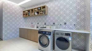 Un lavadero con dos lavadoras de carga frontal, un armario de madera y un estante con objetos decorativos.