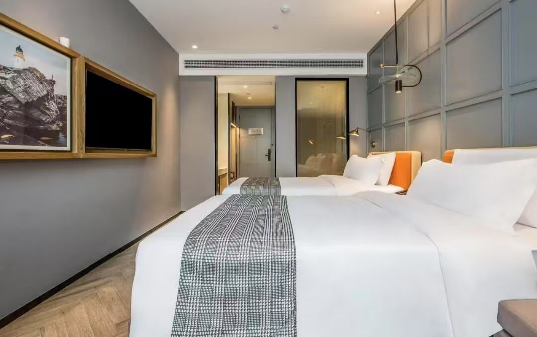 A hotel room with a large bed, a bedside table, a framed picture on the wall, and a view of the hallway.