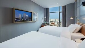 Una habitación de hotel moderna con una cama grande, un televisor montado en la pared y vistas a la ciudad a través de amplias ventanas.