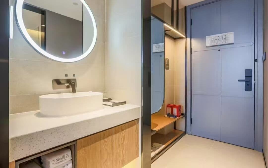 A modern bathroom with a round mirror, a white sink, and a wooden cabinet.
