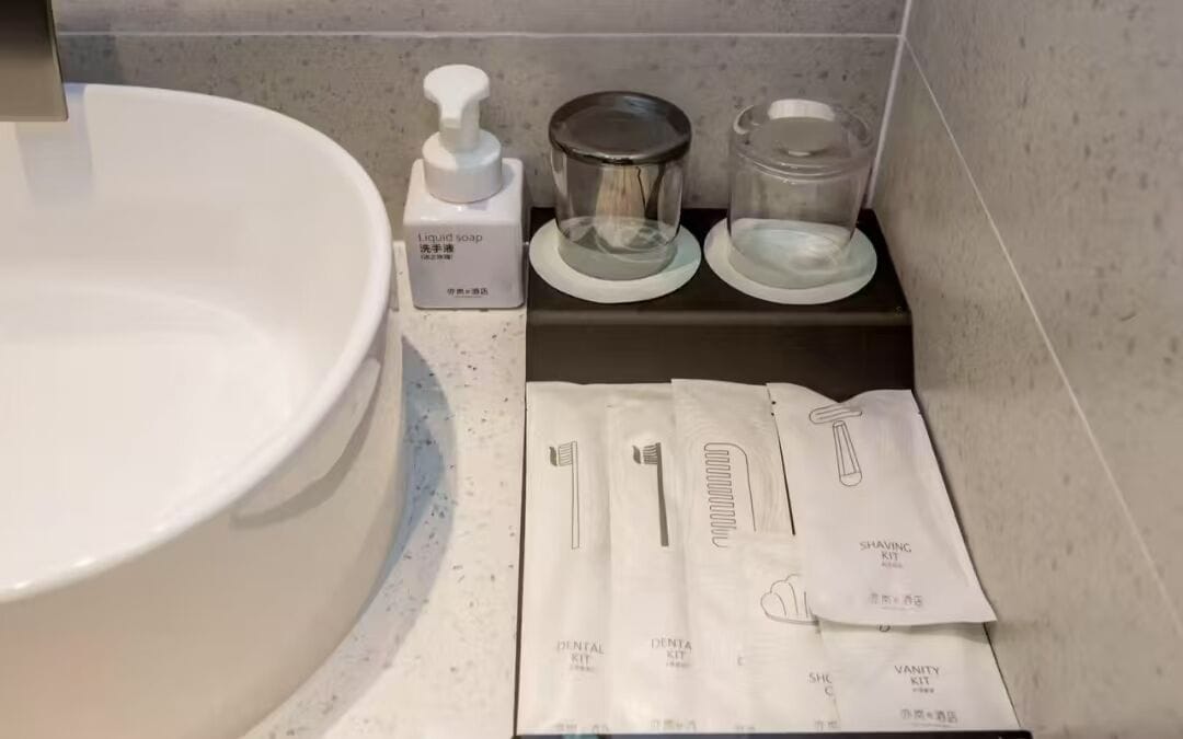 Baño con un lavamanos grande de color blanco, un dispensador de jabón líquido, un kit de afeitar y un recipiente de vidrio.