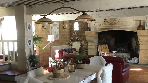A dining area with a white table, clear chairs, and a red sofa. There is a hanging light fixture above the table and a stone fireplace in the background.