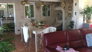 A spacious living area with a red leather sofa, a dining table with chairs, and a kitchen area with a tiled floor.