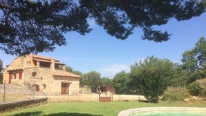 A stone building with a tiled roof, a fenced yard, and a swimming pool.