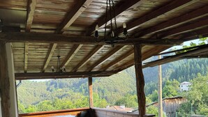 Un espacio al aire libre techado con mesa y sillas, suelo de piedra y vistas a un paisaje boscoso.