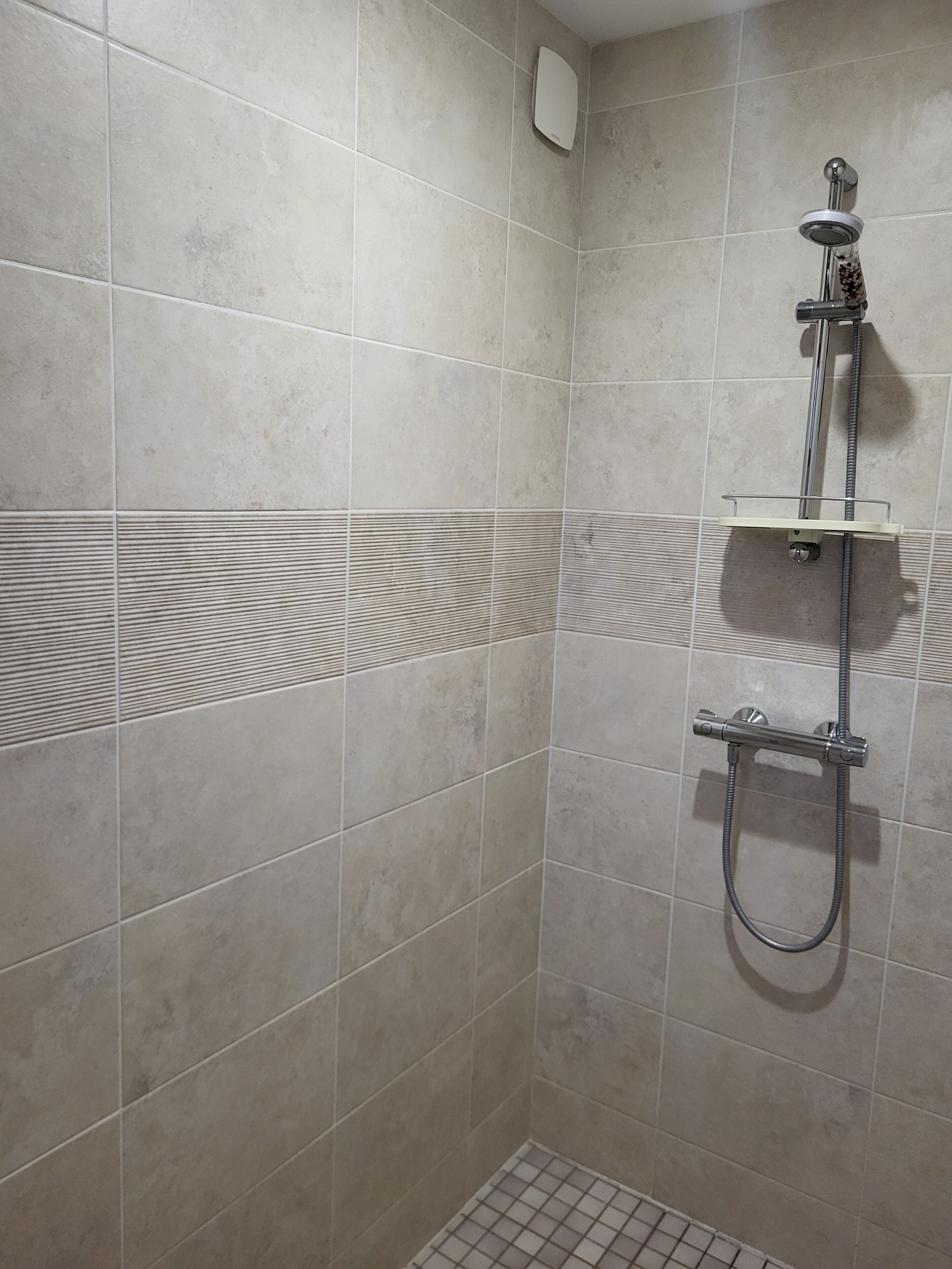 Un espacio de ducha con cabezal de ducha de mano, panel de control empotrado en la pared y repisa.