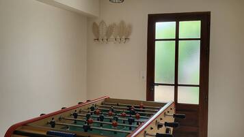 A foosball table in a room with a tiled floor, a wooden door with frosted glass panels, and a ceiling light fixture.