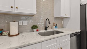 A kitchen with white cabinets, a marble countertop, a stainless steel sink, and a dishwasher. - NEW•Voodoo House•KING Bed• (Lafayette)