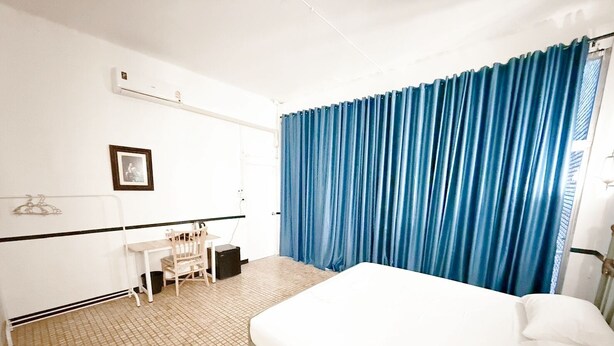 Une chambre d’hôtel avec un lit, un bureau et une chaise. Il y a une fenêtre avec des rideaux bleus.