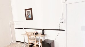 Une petite pièce avec une chaise en bois, une table, une bouilloire et un réfrigérateur noir.