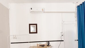 Une petite pièce propre, avec un mur blanc, une chaise en bois, une petite table, une poubelle noire et une porte blanche.